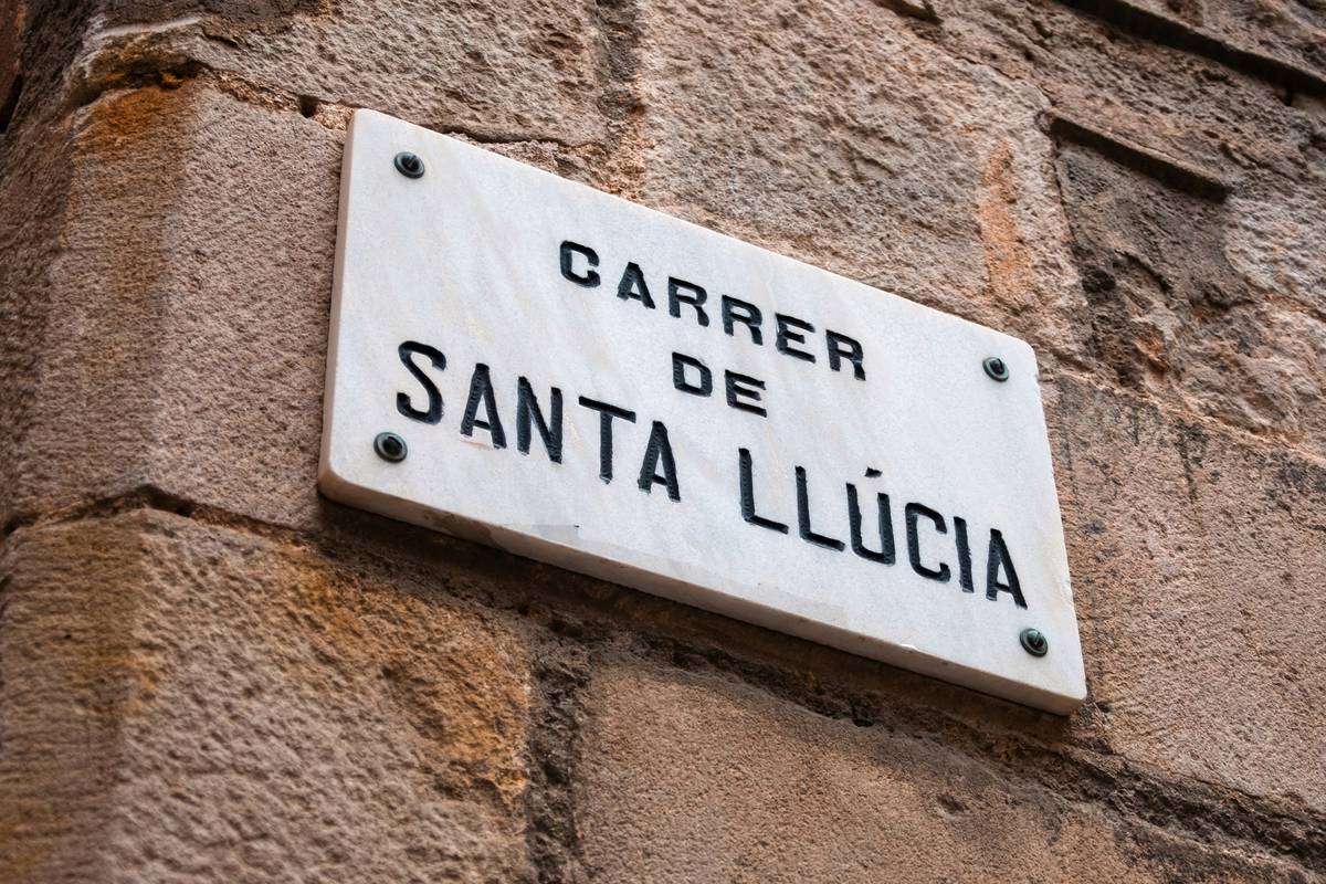 A traveler consulting a bilingual phrase card while standing beside a colorful street sign in Barcelona, showing 'Passeig de Gràcia' — visual aid for how to travel in spanish speaking countries